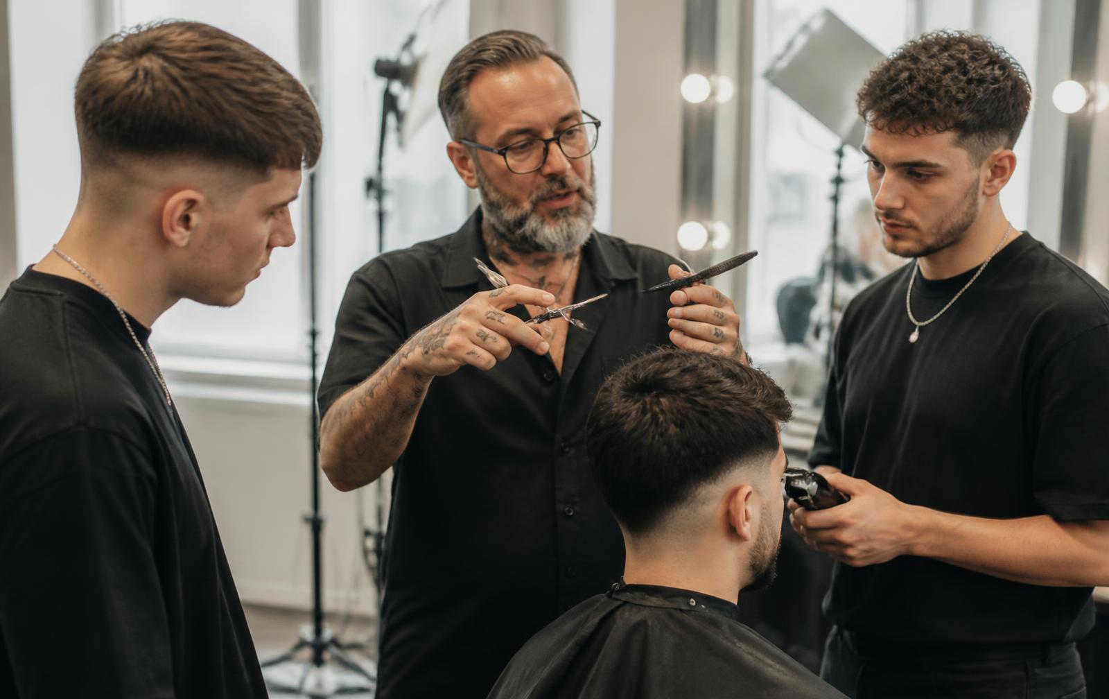 An experienced barber demonstrating a technique to two trainees in a bright UK training studio